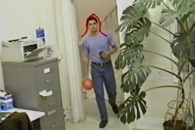 Person entering a room next to an old printer and filing cabinet holding an orange ball