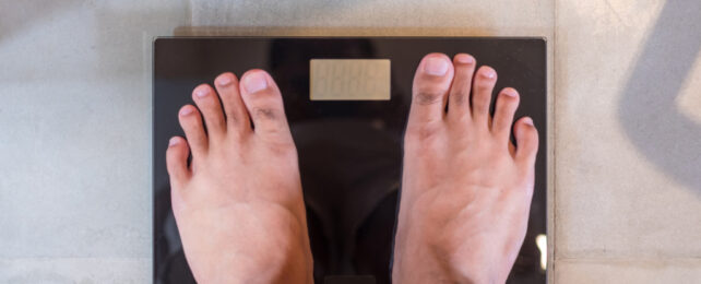 Two feet standing on black, digital weight scales on tiled floor.