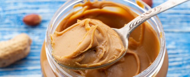 A spoonful of peanut butter rests on top of a jar.
