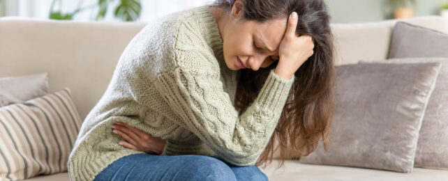 A woman doubled over in pain clutching her stomach and cradling her head in her hand.