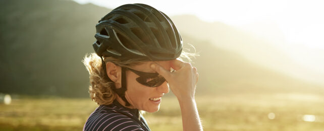 A woman wearing a bicycle helmet and sunglasses cradles her forehead.