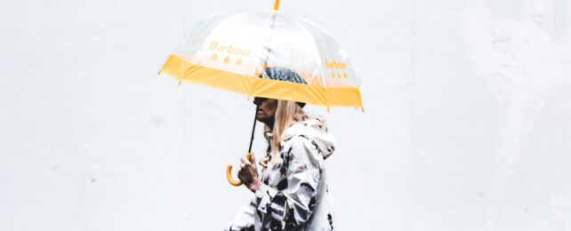A woman walks in the rain while carrying a transparent umbrella.