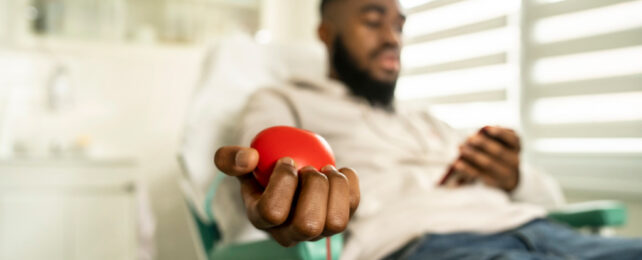 Young black man with beard donating blood while looking at phone.