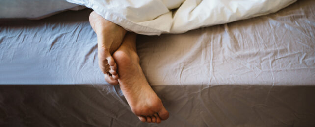 Pair of crossed over feet sticking out of bed sheets.