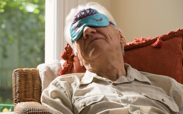 Man Snoozing On a Chair With Bright Blue Eye Mask