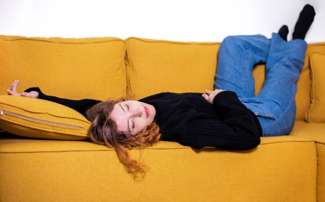Red Haired Person Asleep On A Mustard Yellow Couch
