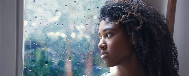 A Black woman staring out a rainy window.