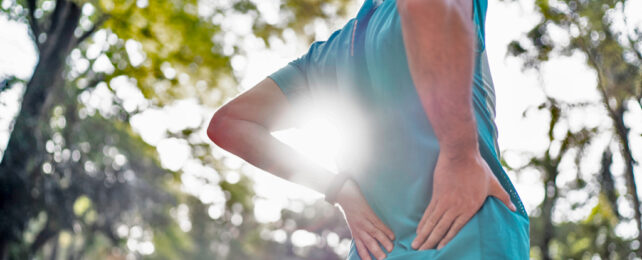 A man supporting his lower back in a park.