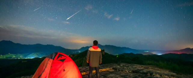 Man stands next to a tent watching shooting stars