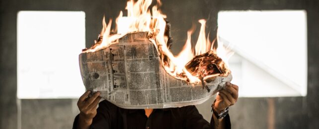 Person Holding Up A Burning Newspaper