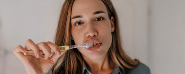 Woman brushing her teeth in the mirror