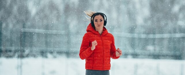 A person wearing headphones and a red puffer jacket running on a snowy day outdoors