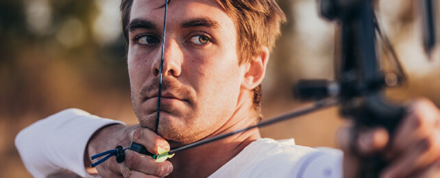 man drawing a string on an archery bow