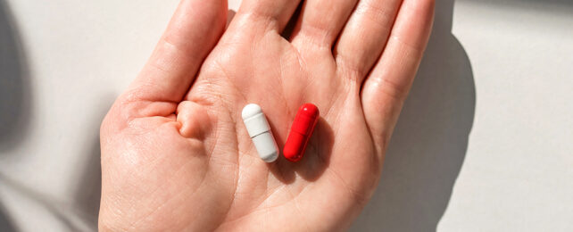 a red pill and a white pill in the palm of a woman's hand