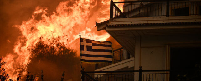 Wildfires burn behind a Greek flag