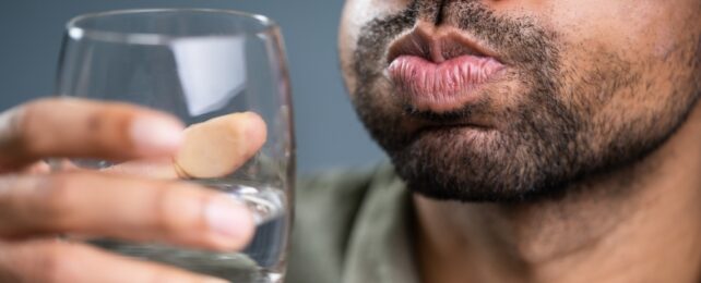 Close view of person's mouth with pursed lips and part of a hand holding a glass