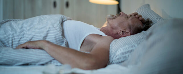 Older man lying awake, resting his hand on forehead.