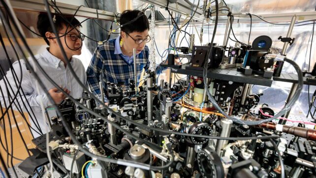 Two male physicists standing behind a machine in physics lab.