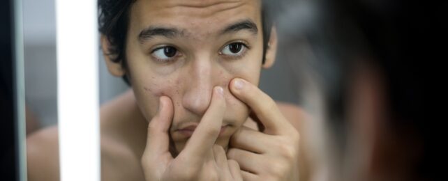 Young Man With Acne Looks In Mirror