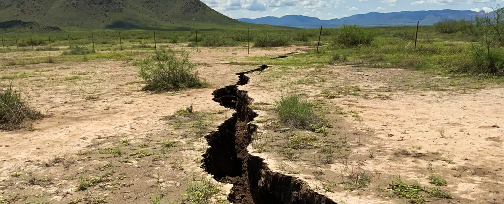 Giant crack splitting a field in Arizona, surrounded by distant hills