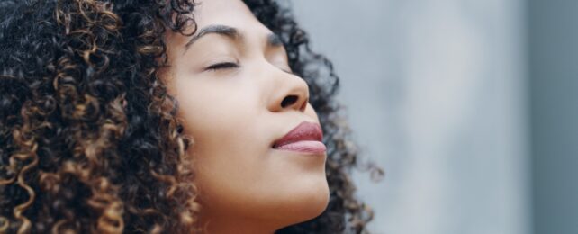 Close up of a dark curly haired lady lifting her face upwards with closed eyes