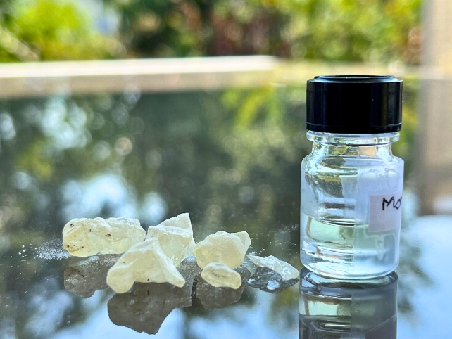 Dammar resin on a glass table next to a bottle of the recreated ancient scent.