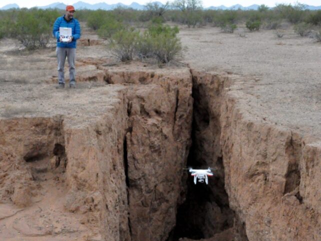 Man standing at edge of deep fissure in ground where drone is descending