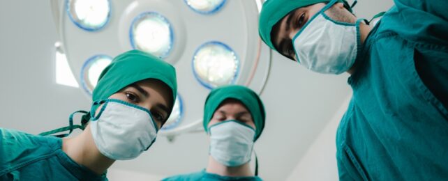 Surgeons in green scrubs and masks looking down