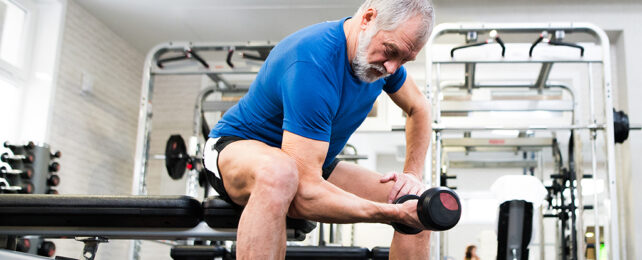 old man in blue shirt lifting single dumb bell