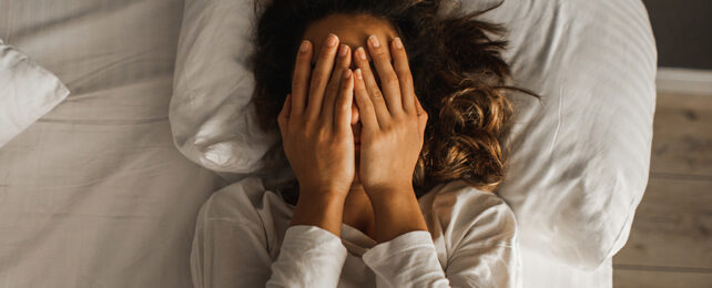 person in bed covering their face