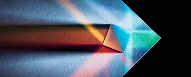 Light refracting through glass prism placed on corner of a white piece of paper.