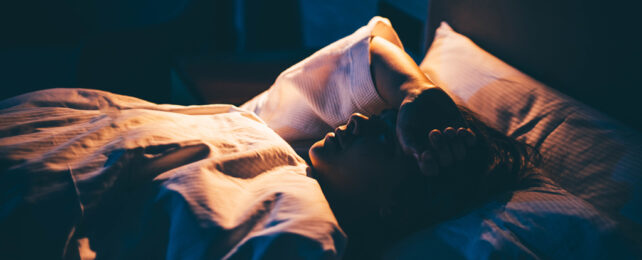 woman lying in bed with arm over head, backlit in warmlight