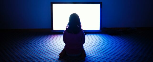 Child Sits In Dark Room Lit By TV