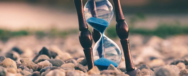 Hourglass running out of blue sand on stony ground
