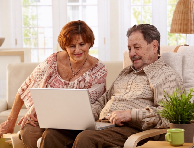 an older women and man on a couch looking down at a laptop