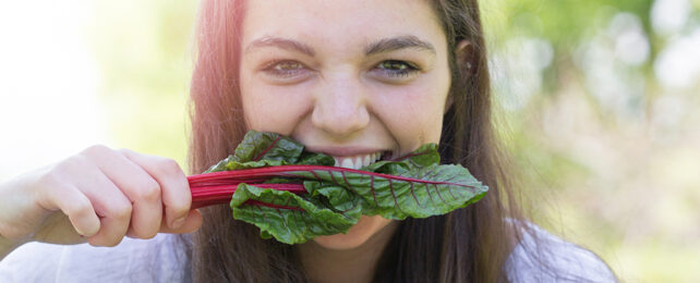 woman with swiss chard held between her teeth