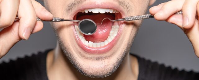 Person holding dental tools next to their open mouth