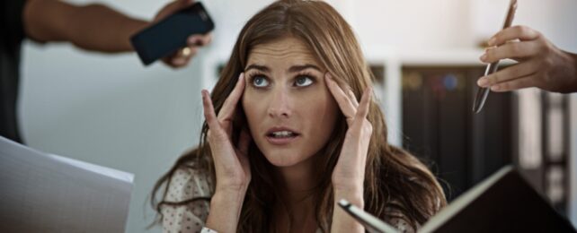 A women with long brown hair looking stressed surrounded by phones and computer