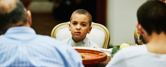 boy sitting at dinner table with a bored expression