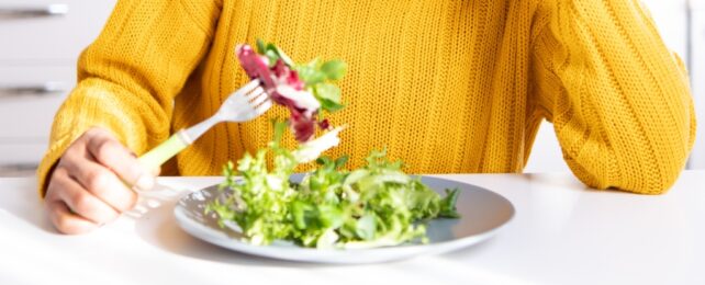 A plate of salad being eaten by someone in a yellow jumper