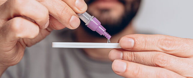 man dripping liquid from small vial into test kit