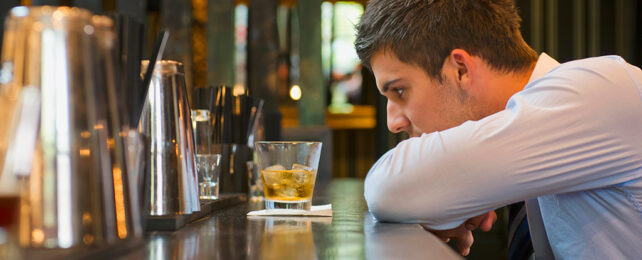 man staring at glass of alcohol at a bar