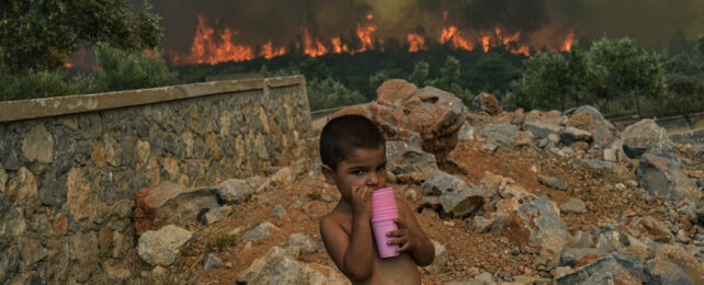 child taking drink as fires blaze behind in Greece