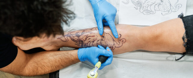 Tattooist wearing blue gloves tattooing an octopus on person's lower leg.