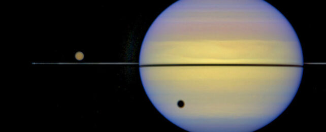 The small dot of Titan casting a shadow on its behemoth of a ringed planet