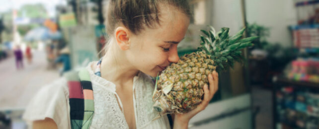 Caucasian women smells pineapple at street market stall.