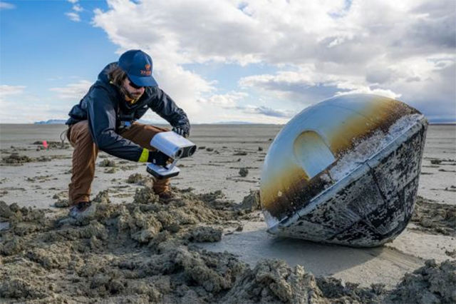 man pointing measuring device at capsule on desert floor