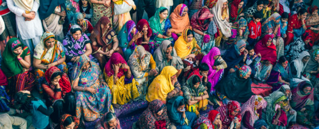 A crowd of Indian women dressed in colourful clothes, sitting on outdoor steps.