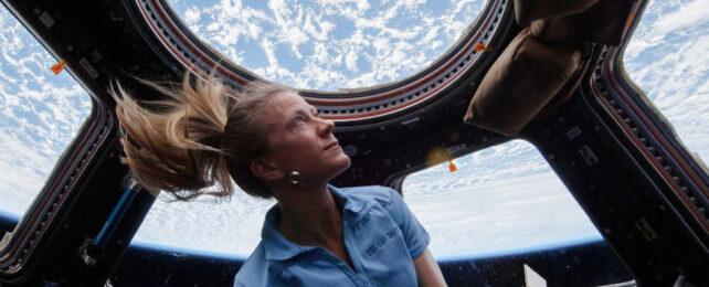 Female astronaut in space looking out window at Earth.