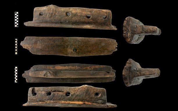 Image of T-shaped wooden pin and four holes in plank of wood used to build a canoe.